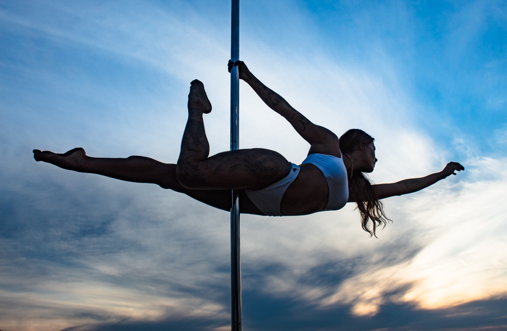 Aluna em movimento no pole ao ar livre, silhueta contra o céu